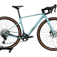 Vélo de gravel Loop Sports Cube Nuroad C:62 ONE 2025 bleu clair avec pneus à flancs marron sur socle en bois