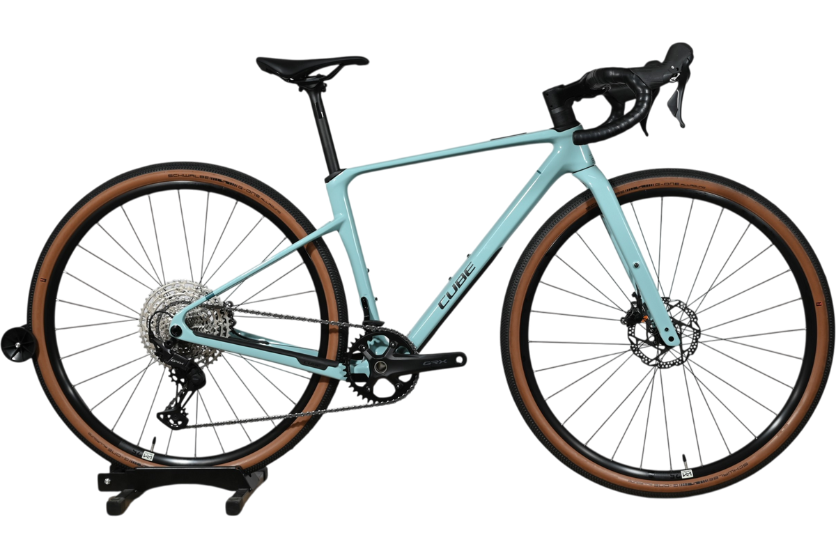 Vélo de gravel Loop Sports Cube Nuroad C:62 ONE 2025 bleu clair avec pneus à flancs marron sur socle en bois