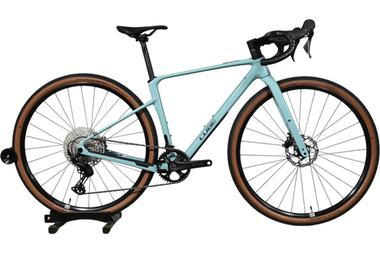 Vélo de gravel Loop Sports Cube Nuroad C:62 ONE 2025 bleu clair avec pneus à flancs marron sur socle en bois