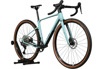 Velo gravel Loop Sports Cube Nuroad C:62 ONE 2025 bleu clair avec pneus a flancs marron sur support en bois