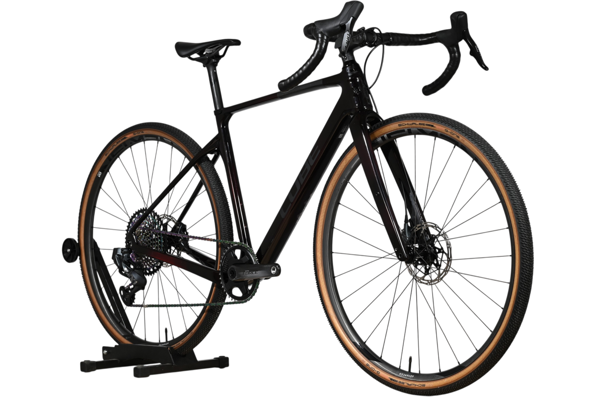 Vélo de gravel Loop Sports Cube Nuroad C:62 SLT noir en carbone avec pneus à flancs beiges sur support en bois