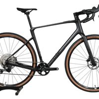 Vélo de gravel Loop Sports Cube Nuroad C:62 ONE 2025 noir mat avec pneus à flancs marron sur socle en bois