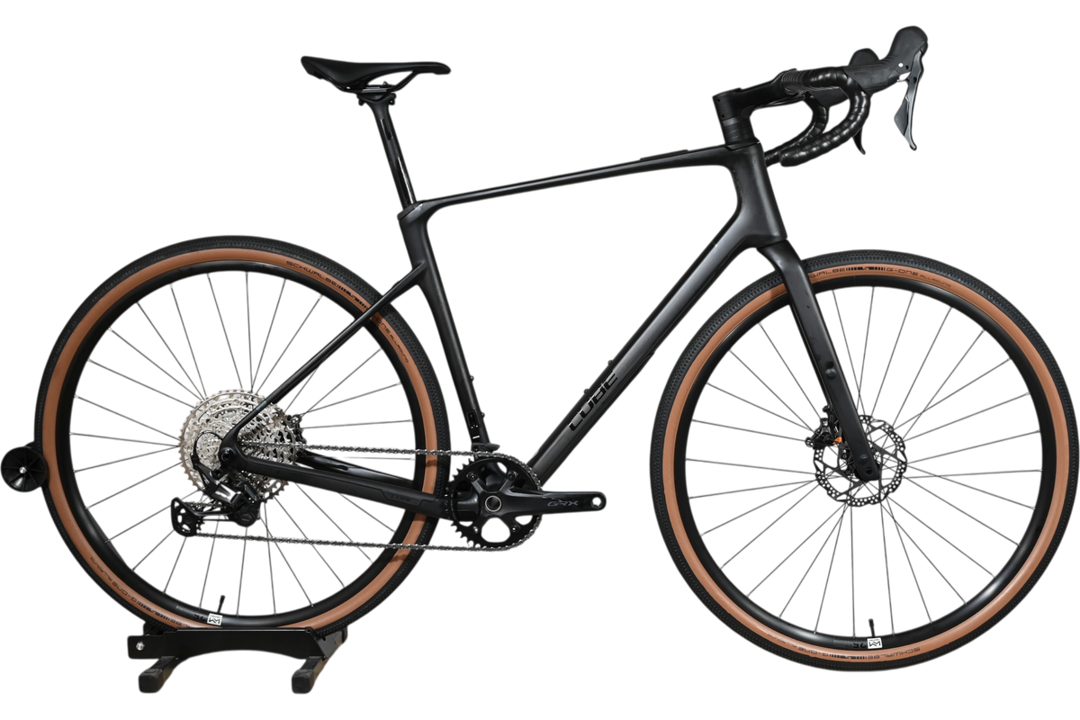 Vélo de gravel Loop Sports Cube Nuroad C:62 ONE 2025 noir mat avec pneus à flancs marron sur socle en bois