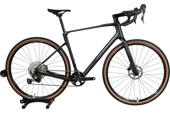 Vélo de gravel Loop Sports Cube Nuroad C:62 ONE 2025 noir mat avec pneus à flancs marron sur socle en bois