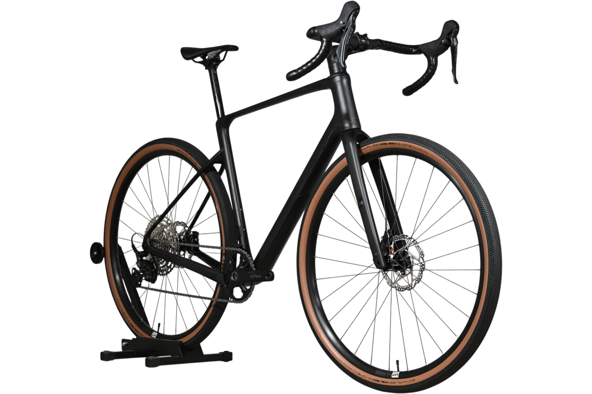 Vélo de gravel Loop Sports Cube Nuroad C:62 ONE 2025 noir mat avec pneus à flancs marron sur support en bois