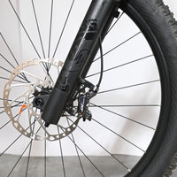 Gros plan sur la roue avant, la fourche noire et le frein à disque hydraulique du vélo Loop Sports Cube Stereo Hybrid