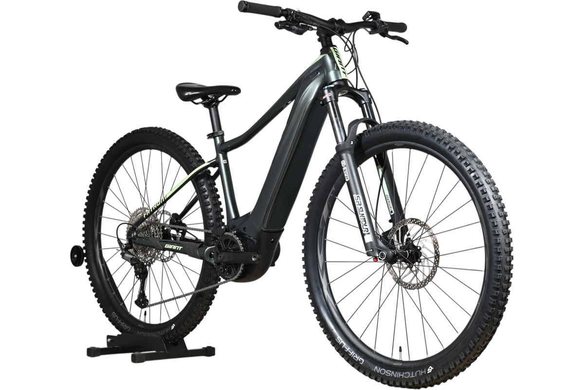 Velo electrique VTT Loop Sports Giant Fathom E+1 2022 gris fonce avec pneus tout-terrain sur support en bois
