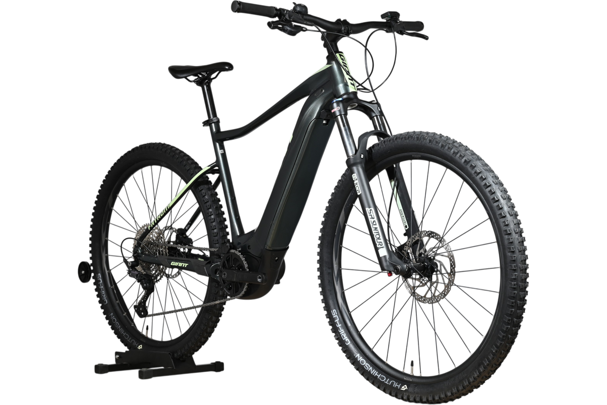 VTT électrique Giant Fathom E+1 Loop Sports noir avec accents vert lime, monté sur un support en bois