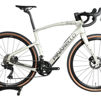 Vélo de gravel Loop Sports Pinarello Grevil F1 GRX 2x12 2026 blanc cassé avec pneus à flancs beiges sur socle en bois