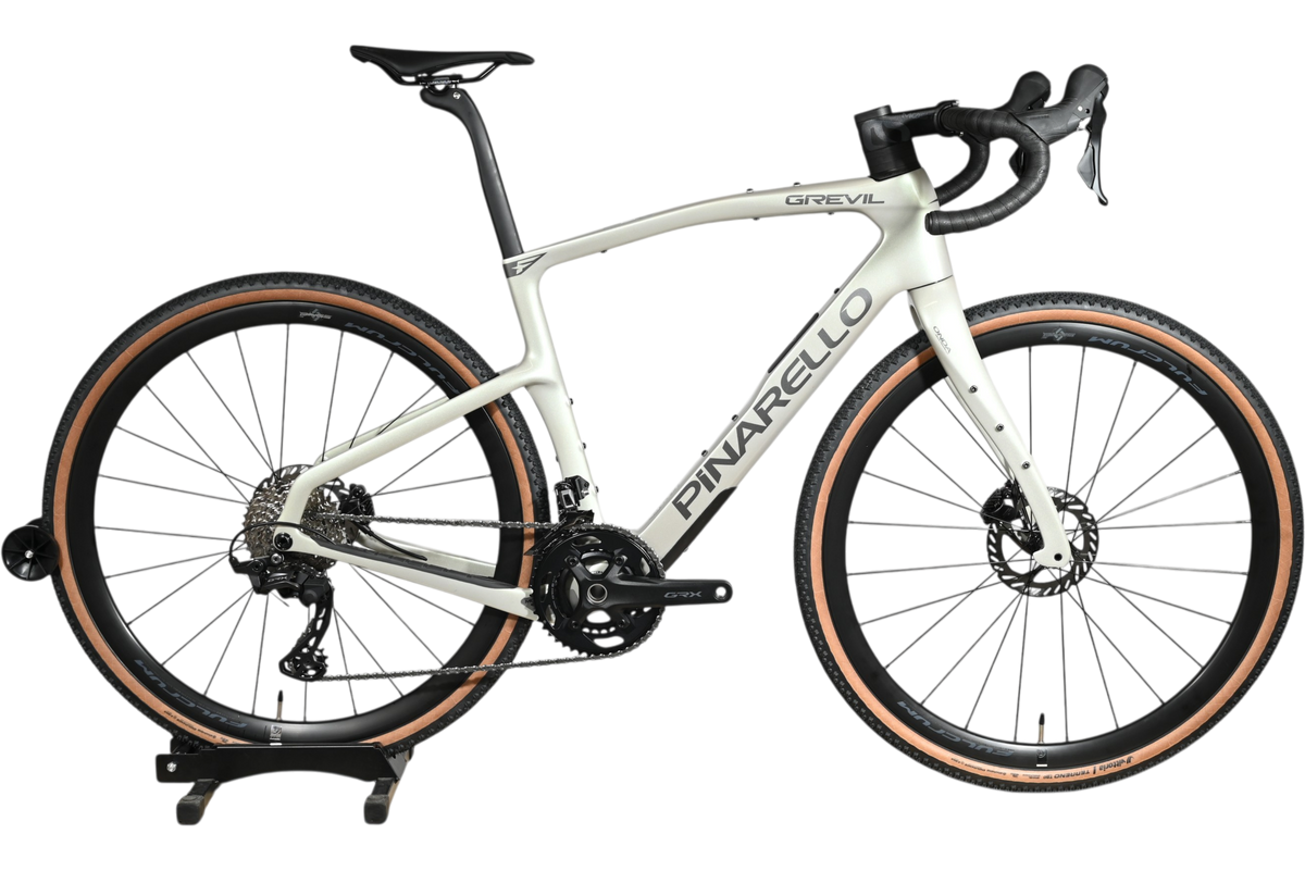 Vélo de gravel Loop Sports Pinarello Grevil F1 GRX 2x12 2026 blanc cassé avec pneus à flancs beiges sur socle en bois