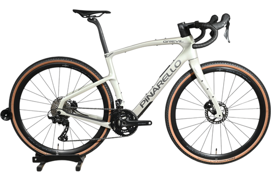 Vélo de gravel Loop Sports Pinarello Grevil F1 GRX 2x12 2026 blanc cassé avec pneus à flancs beiges sur socle en bois