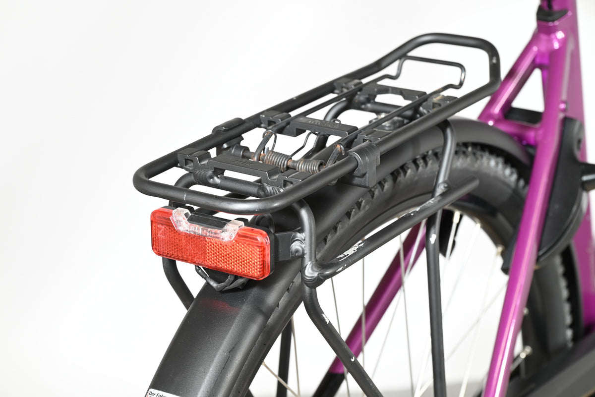 Porte-bagages noir avec feu arrière rouge sur vélo électrique violet Victoria Trekking 11.5 de Loop Sports