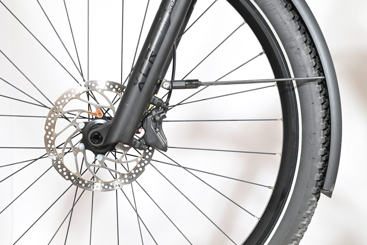 Gros plan sur la roue avant et le frein à disque du vélo Scott Axis 10 de Loop Sports avec garde-boue noir