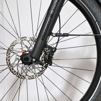 Gros plan sur la roue avant, le frein à disque et la fourche suspendue Suntour du vélo Loop Sports Scott Sub Tour 10