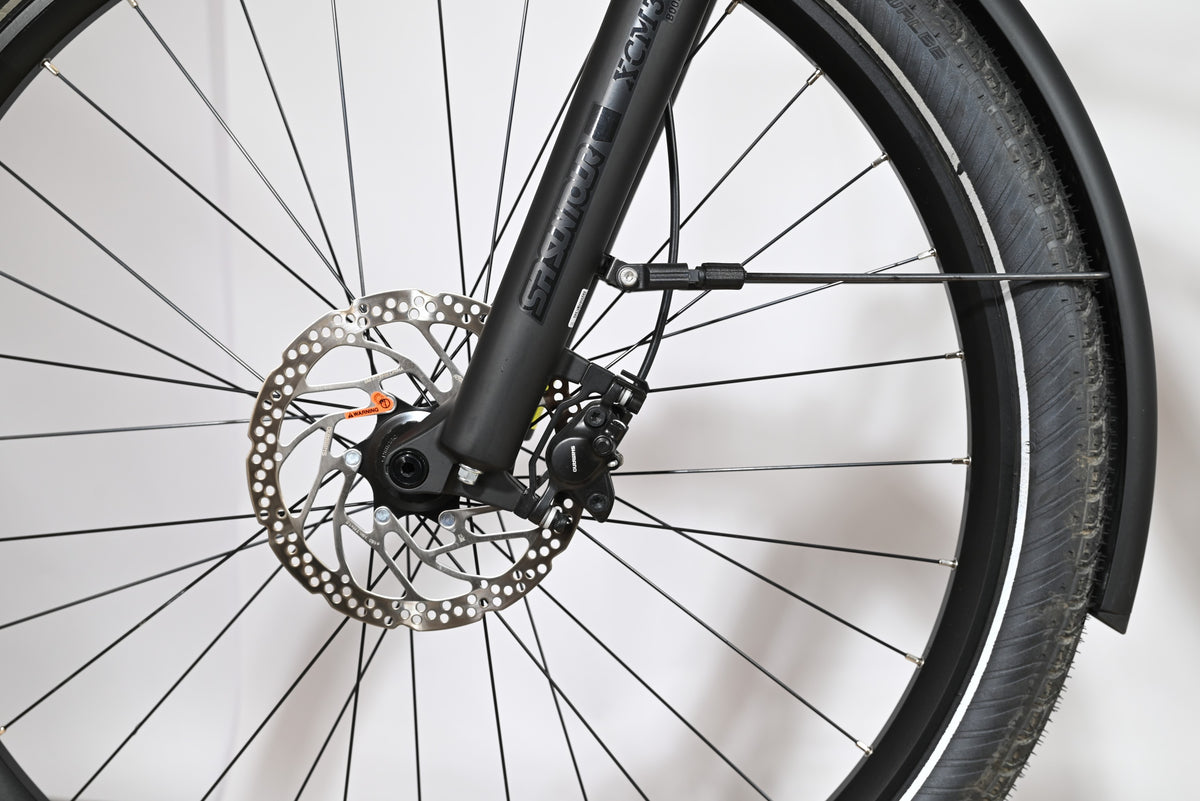 Gros plan sur la roue avant, le frein à disque et la fourche suspendue Suntour du vélo Loop Sports Scott Sub Tour 10