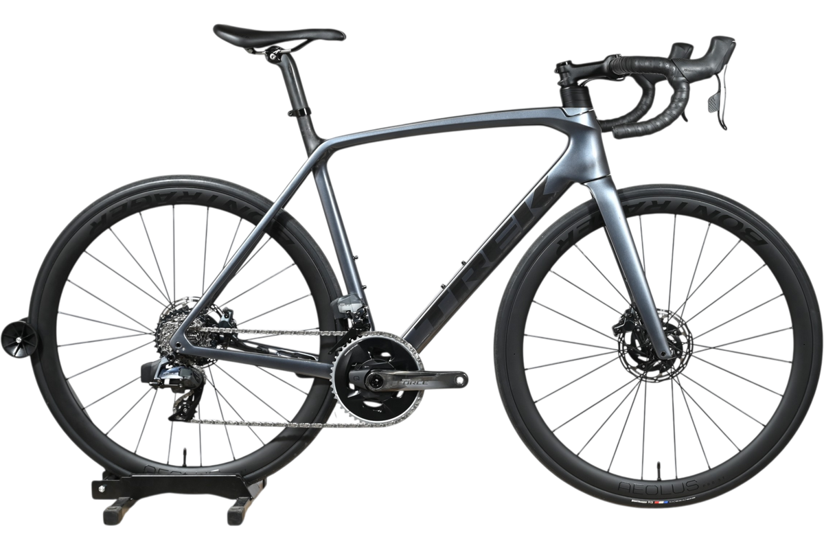Vélo de route Trek Emonda SL7 AXS 2023 gris carbone chez Loop Sports sur un support en bois