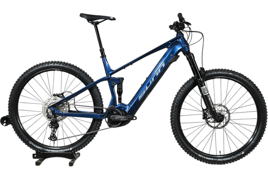 VTT électrique Sunn Charger S1 2025 bleu avec suspension intégrale, présenté par Loop Sports sur un socle en bois.